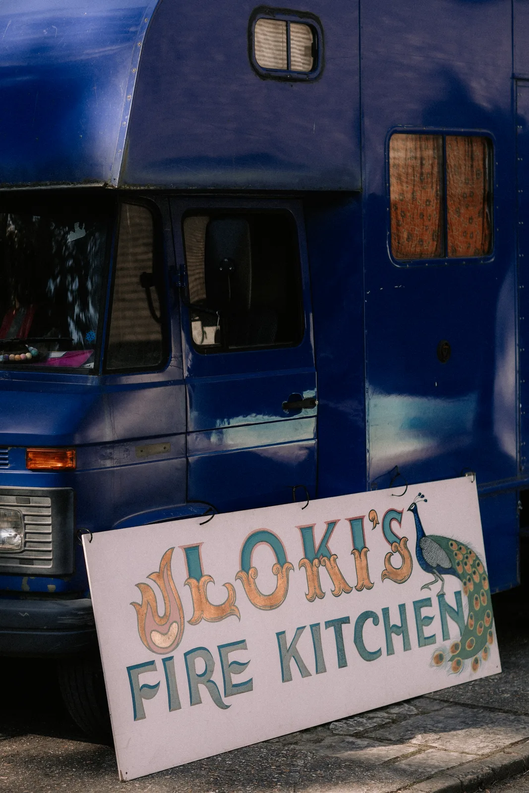 A hand-painted Loki's Fire Kitchen sign propped against a blue van.