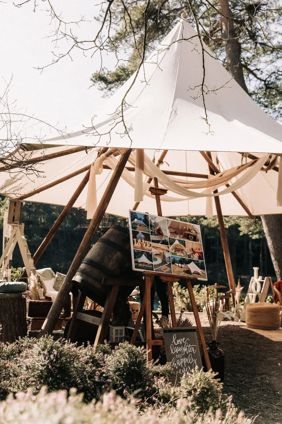 Photo boards on easels under the tipi, the lake bright behind.