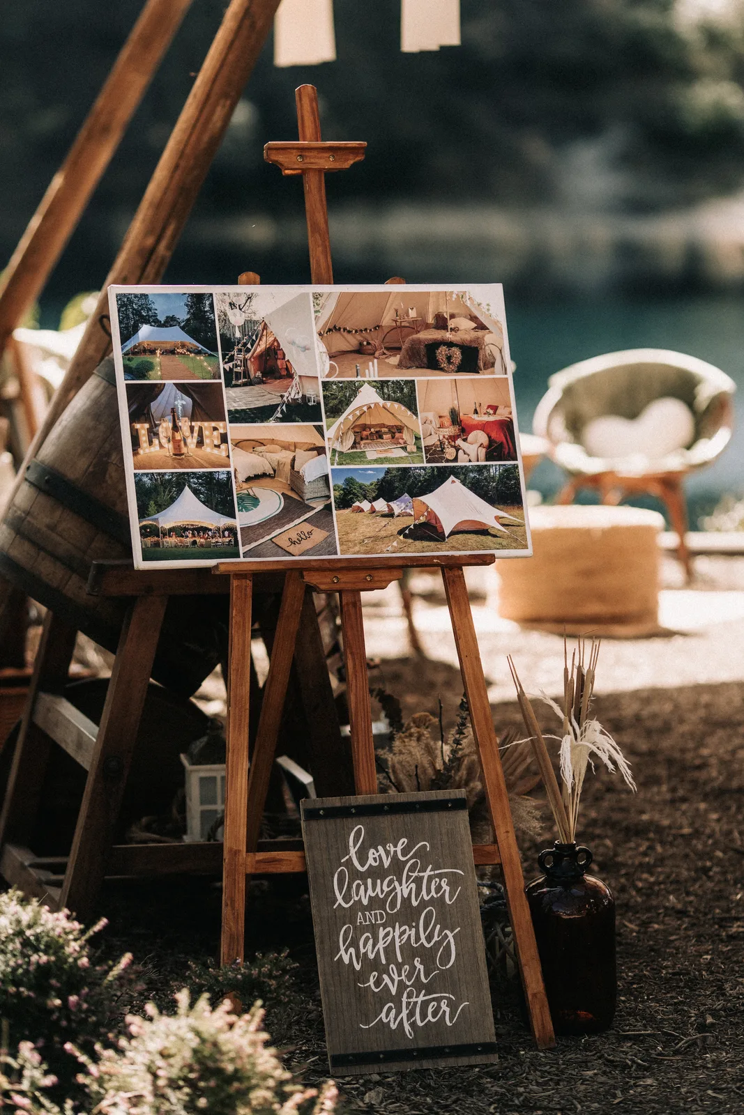 An easel of wedding photographs and a chalk sign beside wicker chairs under the tipi.