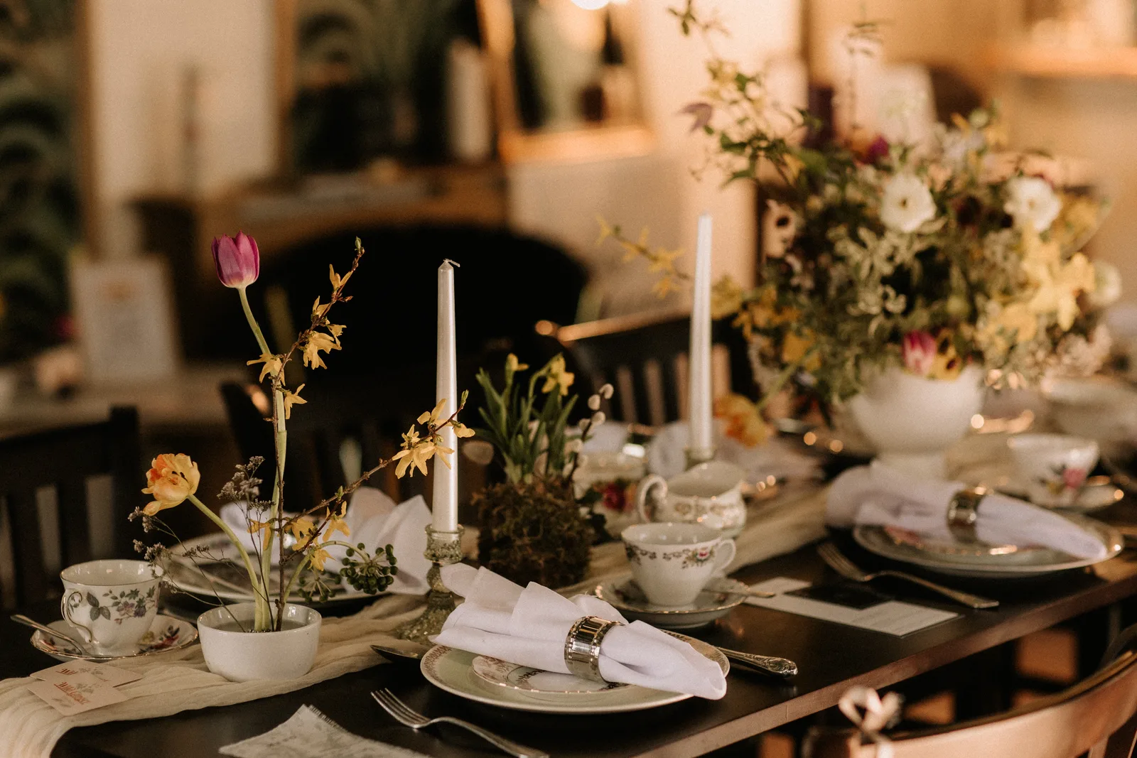 A laid table with spring flowers, candles and vintage china by the tea room window.