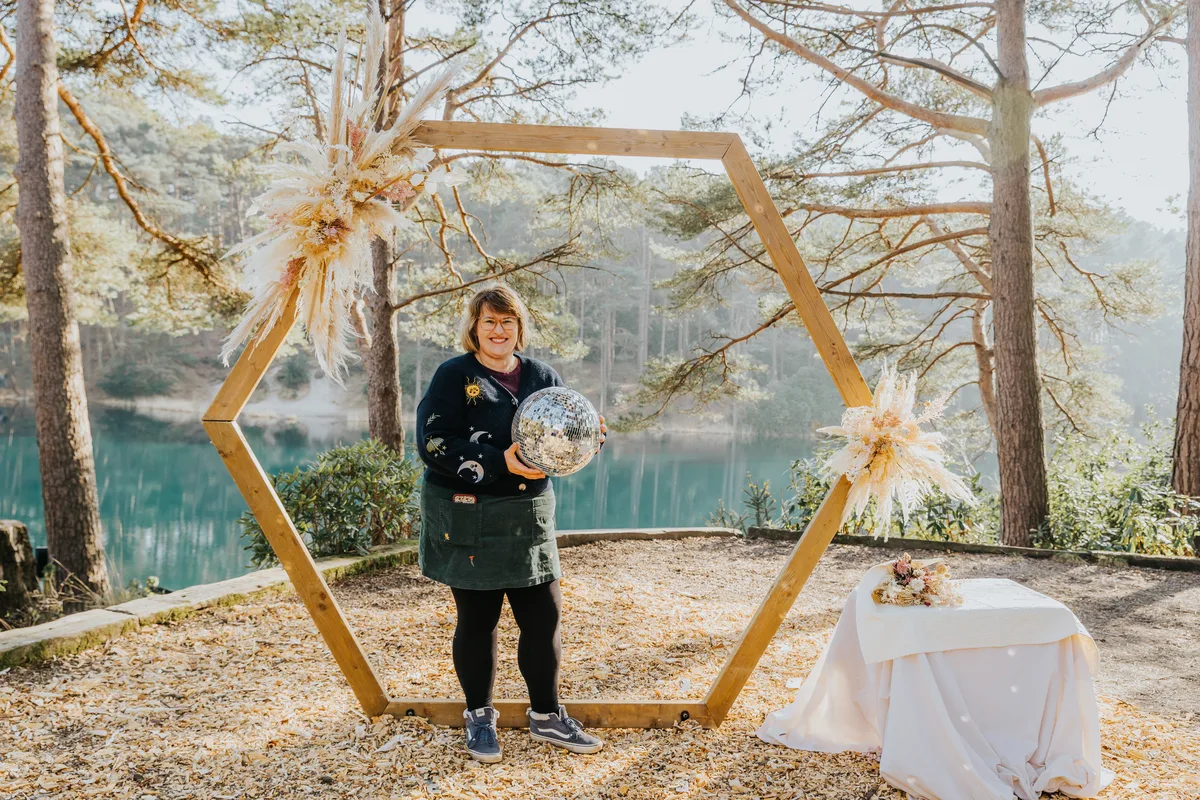 Gemma holding a disco ball under the wooden arch, in a starry cardigan and green skirt.